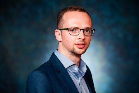 Headshot of Armin Langer in a blue jacket, light blue shirt in front of dark background