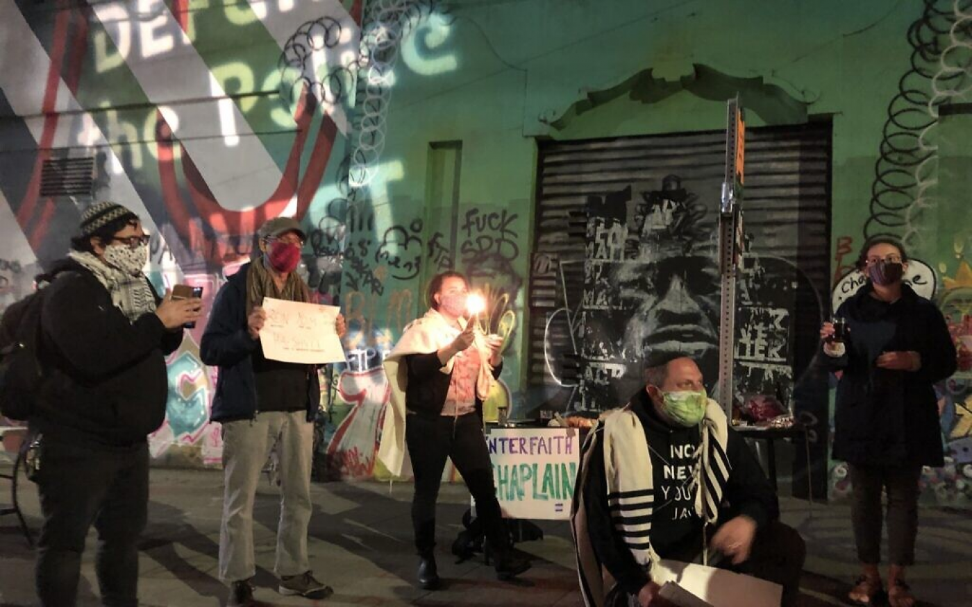 Rabbi David Basior, kneeling, leads the havdallah prayer in the Capital Hill Autonomous Zone, as Kayla Jackson, right, holds the wine, June 13, 2020.