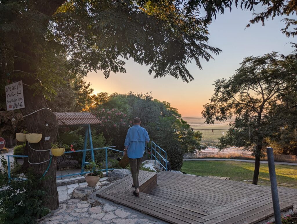 Person walking on a terrace with trees and sea view at sunset.