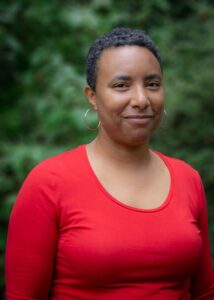 Amanda Mbuvi, wearing a red shirt, poses in front of trees outside RRC's building.