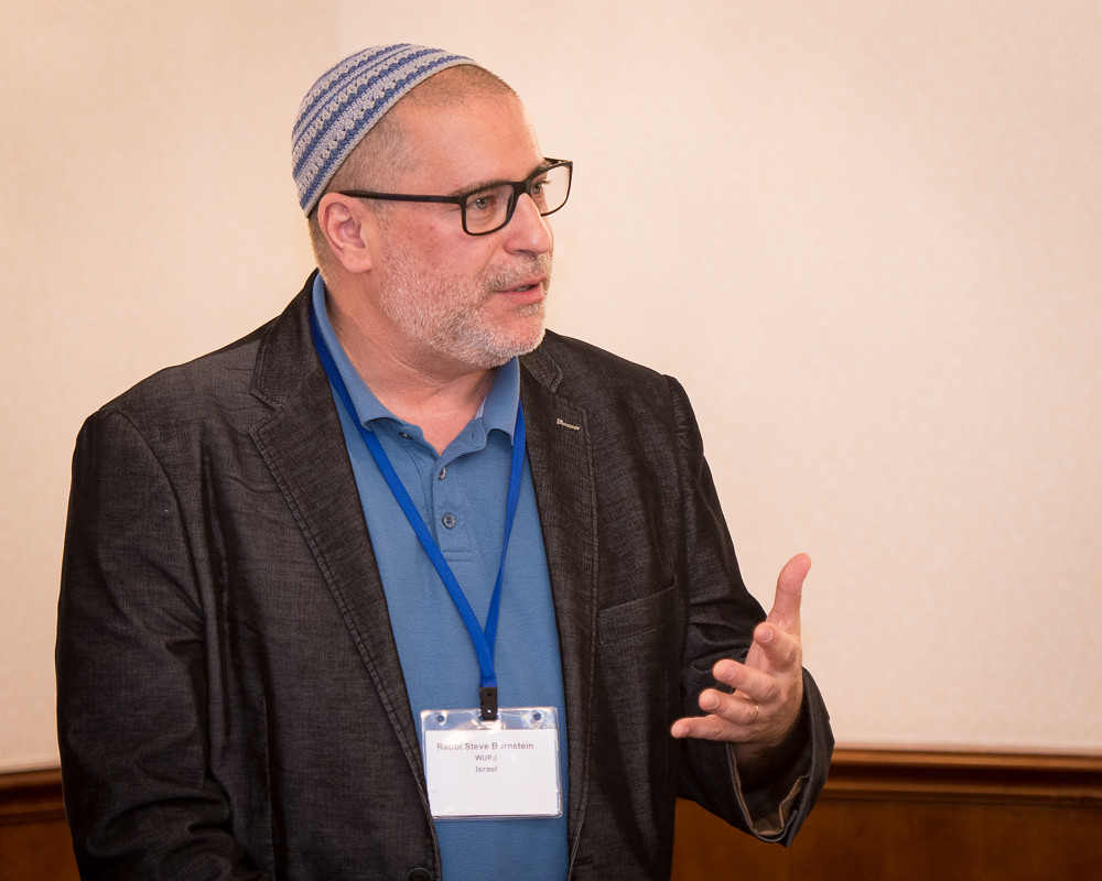 Rabbi Steve Burnstein, wearing a polo and blazer, delivers a talk