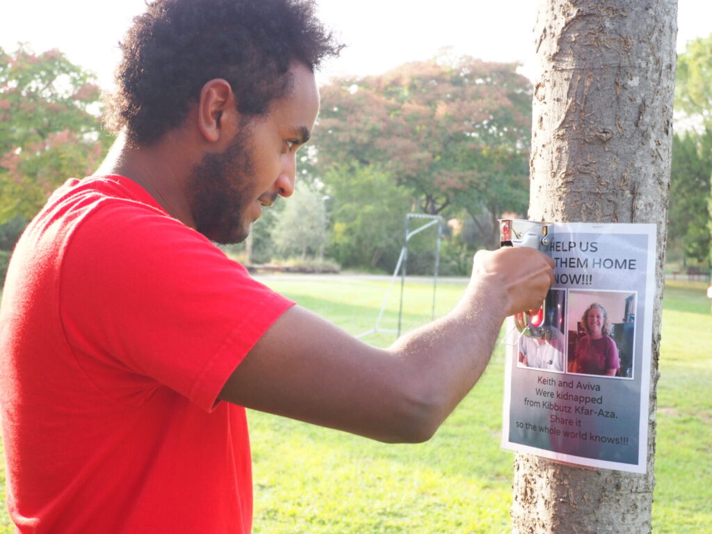 An Ethopian-Israeli man wearing a short-sleeved red shirt posts a picture of a missing hostage on a telephone poll.