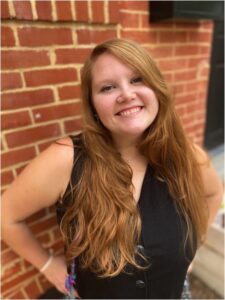 Rabbi Shira Singelenberg, with long red hair and smiling, stands in front of a brick wall outside RRC.