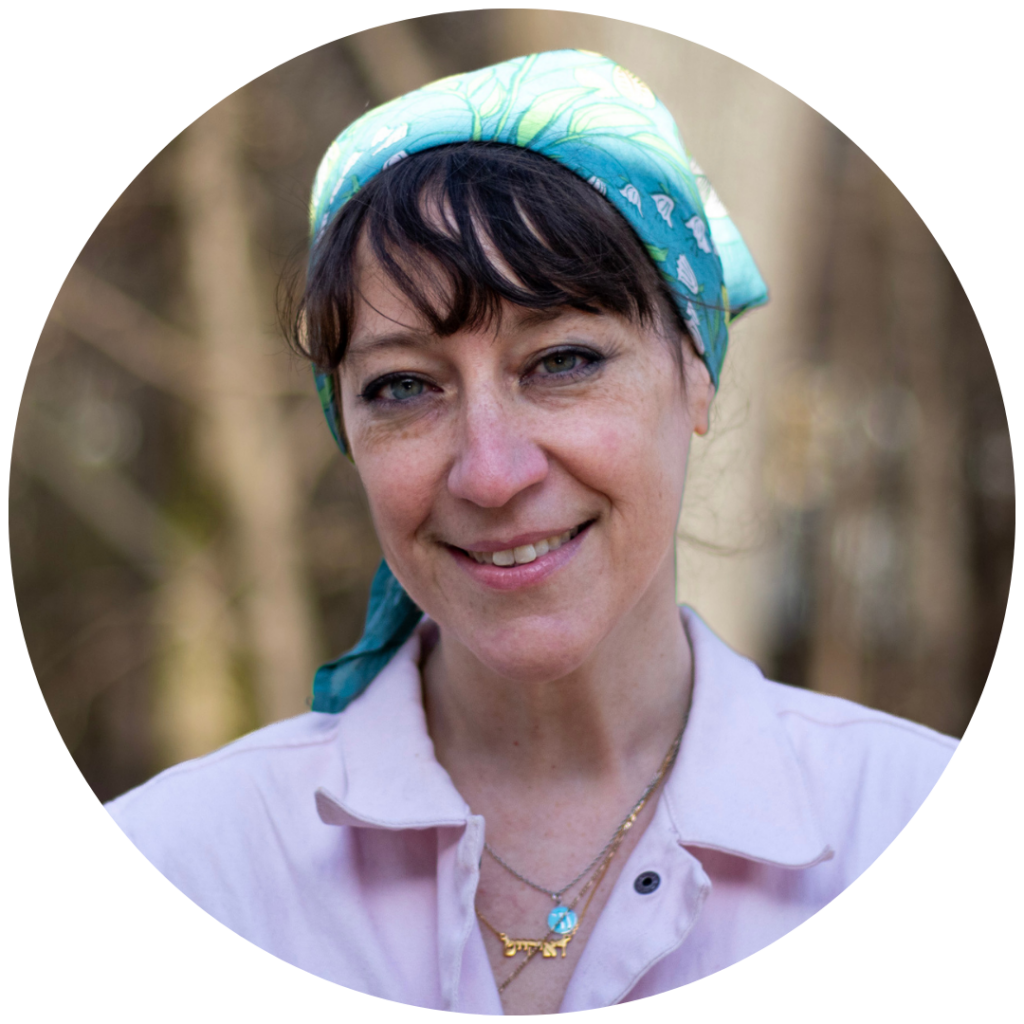 Woman with a blue headscarf smiling outdoors, wearing a pink shirt and layered necklaces.