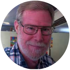A bearded man wearing glasses and a plaid shirt smiles at the camera.