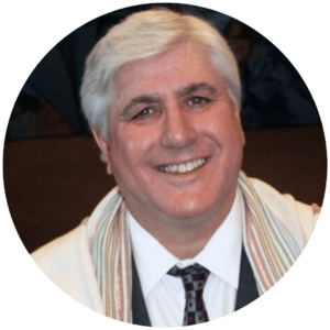 Smiling man with short gray hair wearing a suit and tie, with a colorful scarf draped over his shoulders.