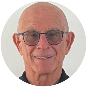 Elderly man with glasses, smiling, against a plain white background.