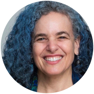 Smiling person with curly blue-gray hair and earrings, facing forward.