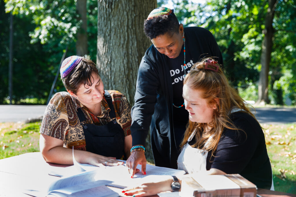 Three people study together at an outdoor table, engaged in discussion.