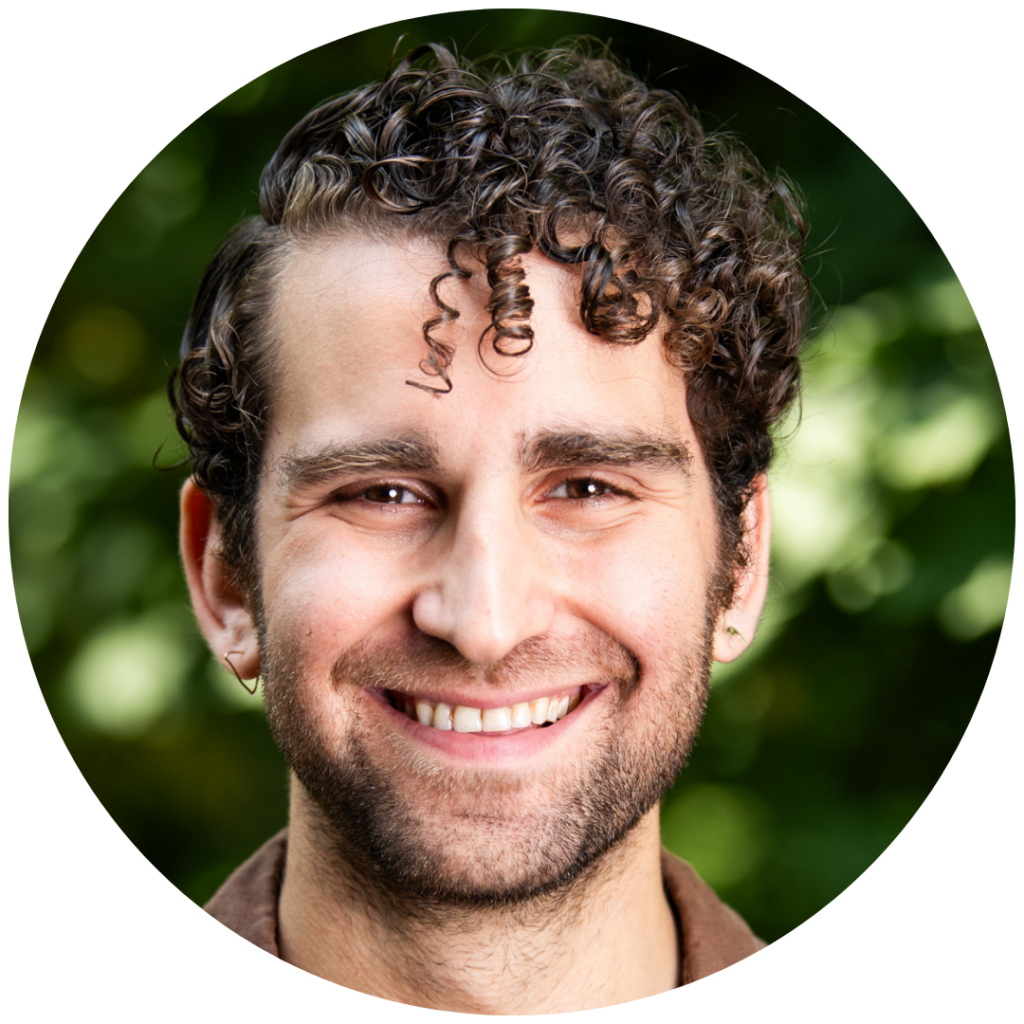 Smiling person with curly hair and earrings, outdoors with a blurred green background.