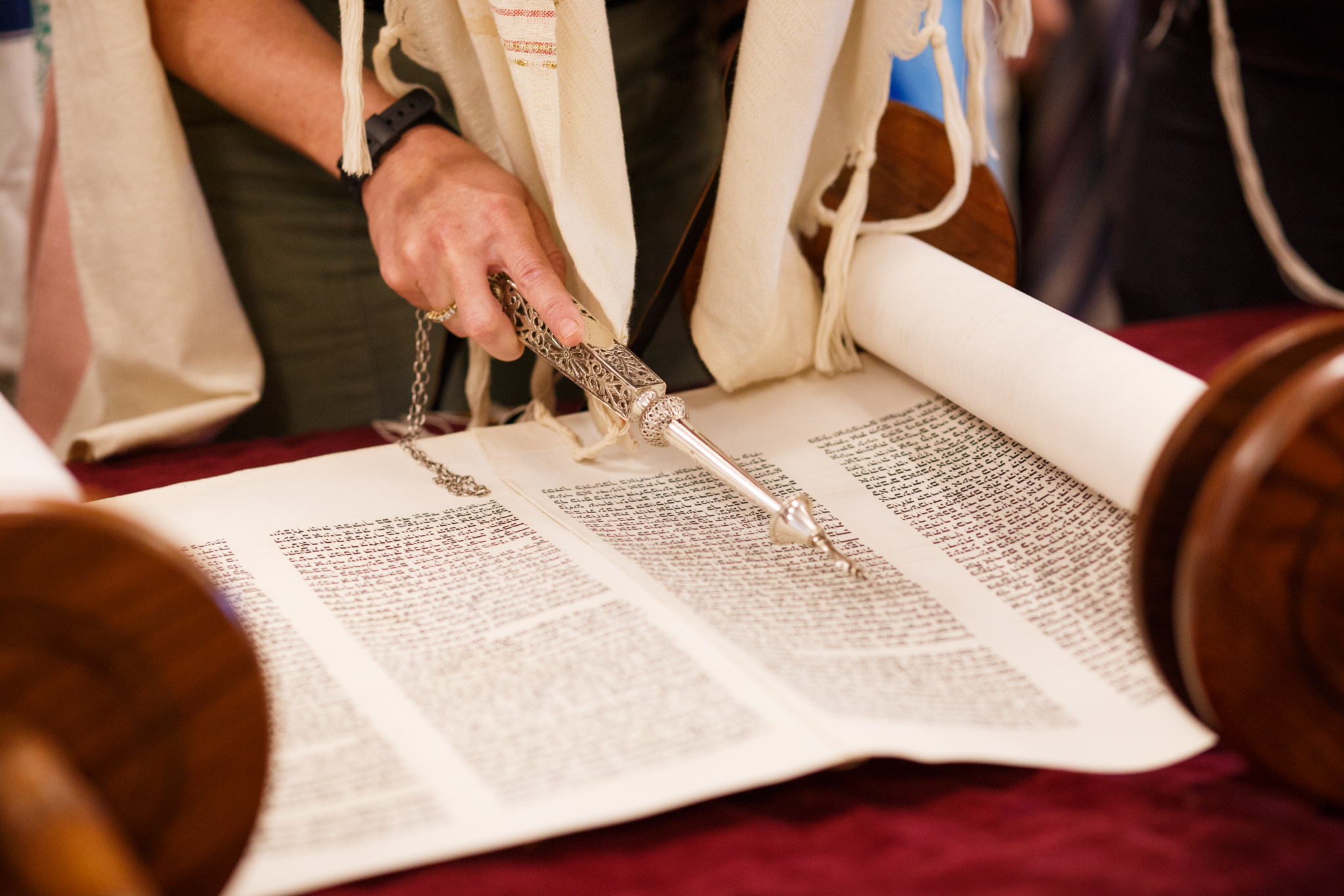 A person uses a silver yad pointer to read from an open Torah scroll on a table.