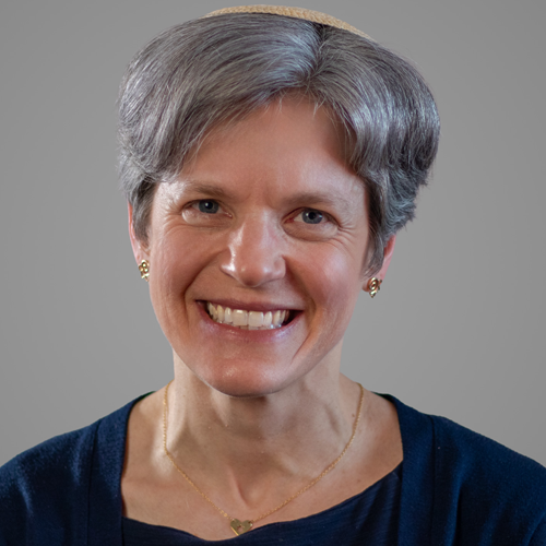 Smiling woman with short gray hair, wearing a navy top and gold necklace, against a gray background.