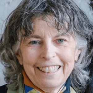 An older woman with gray, wavy hair smiles at the camera, wearing a colorful scarf.