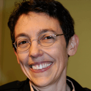 A person with short dark hair and glasses smiling in front of a yellow background.