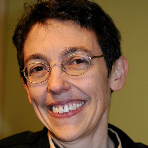 A person with short dark hair and glasses smiling in front of a yellow background.