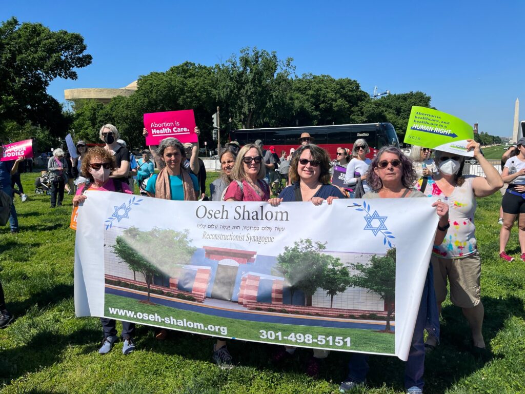 A group holds an Oseh Shalom banner at an outdoor rally; some hold signs supporting abortion rights.
